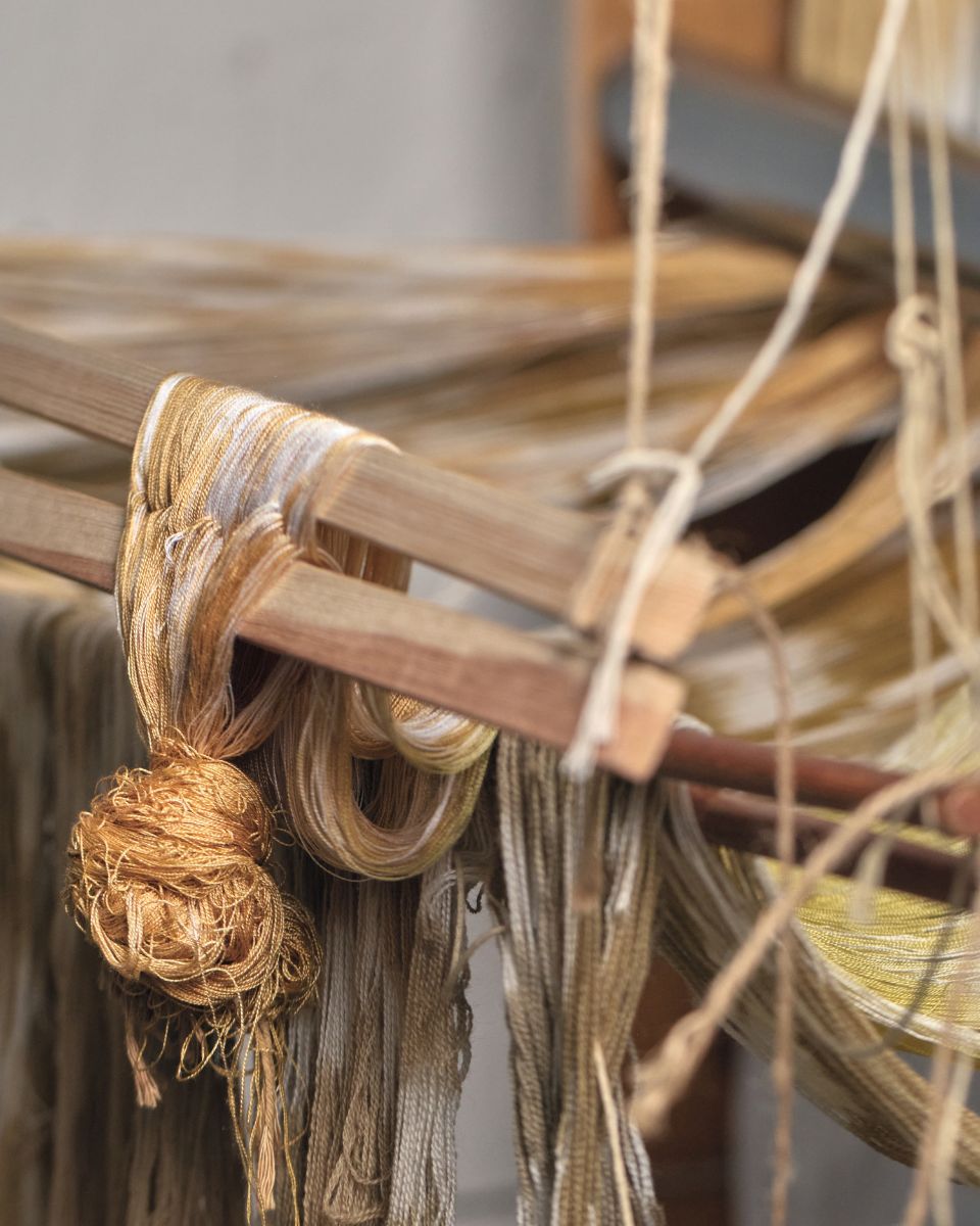 Close-up of golden and olive-green warp threads wound onto a wooden weaving floor loom.
