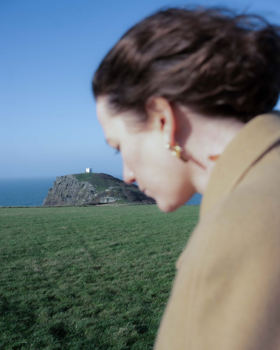 Outdoor portrait of artist Julianna Byrne framed by the rugged coast and sea landscape of Cornwall.