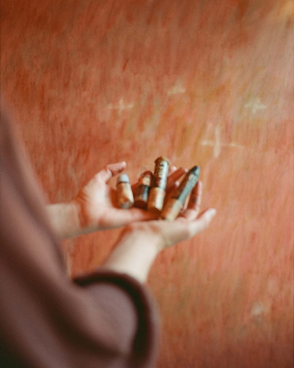Close-up of artist Julianna Byrne’s hands holding vibrant wax crayons in front of one of her paintings for Partnership Editions.
