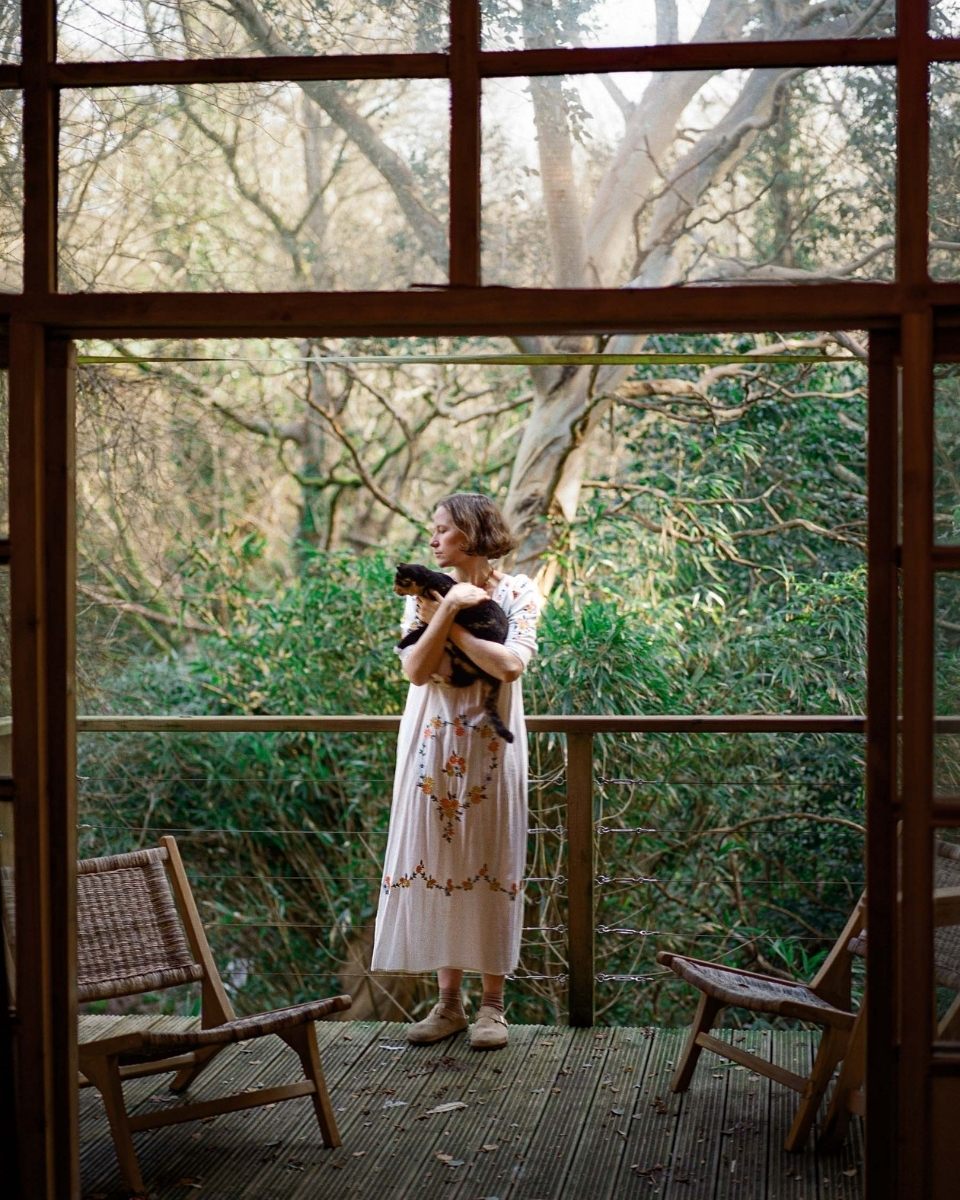 Full-length portrait of painter Julianna Byrne standing on her balcony while holding her pet cat.