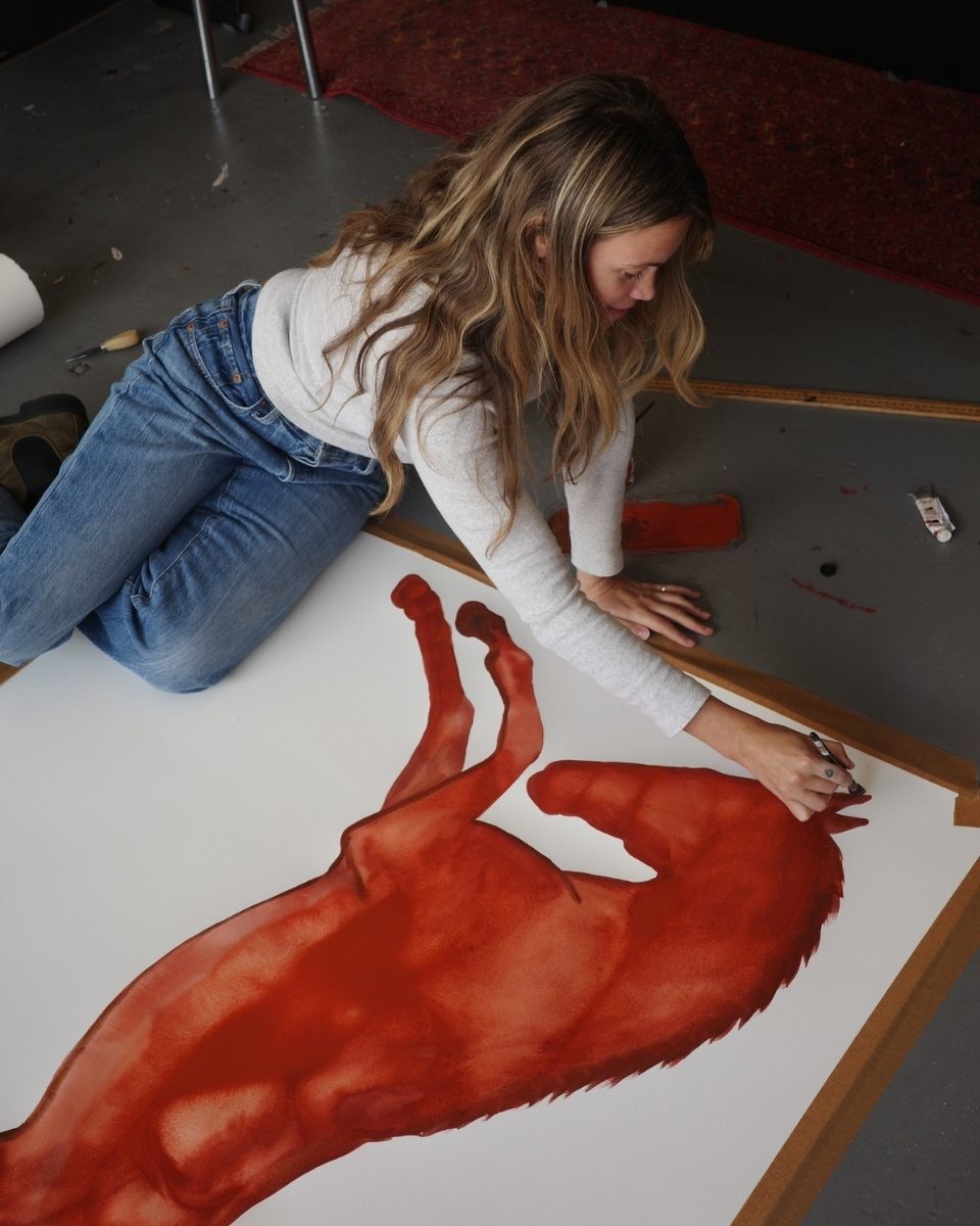 Artist Kara Marshall working on her studio floor, painting an expressive red horse watercolour for Partnership Editions.