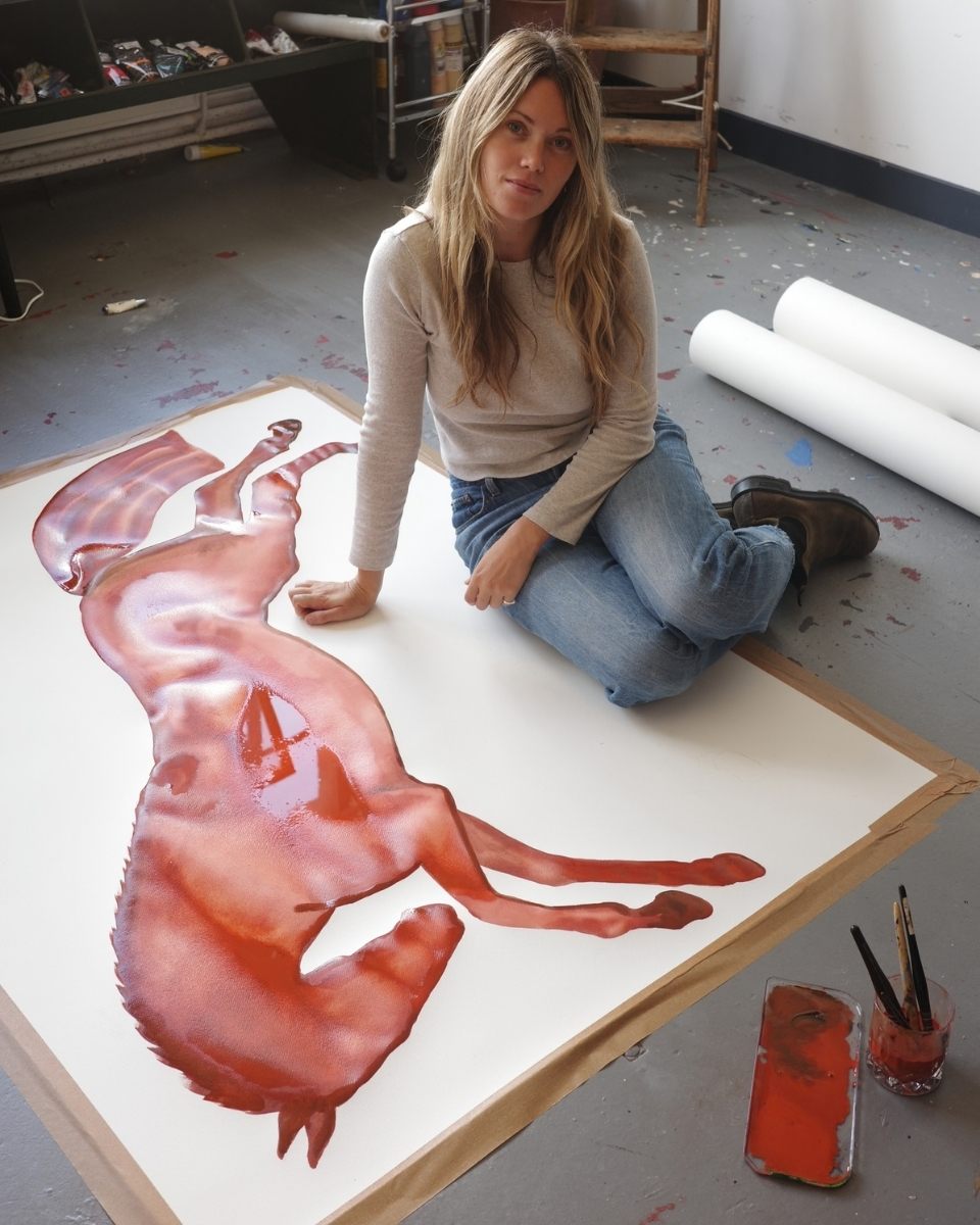 Artist Kara Marshall posing in her studio next to a wet, drying watercolour horse painting.