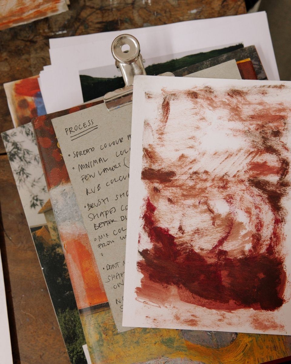 Stacked process notes, landscape sketches, and reference imagery on artist Katarina Lalic's studio desk.