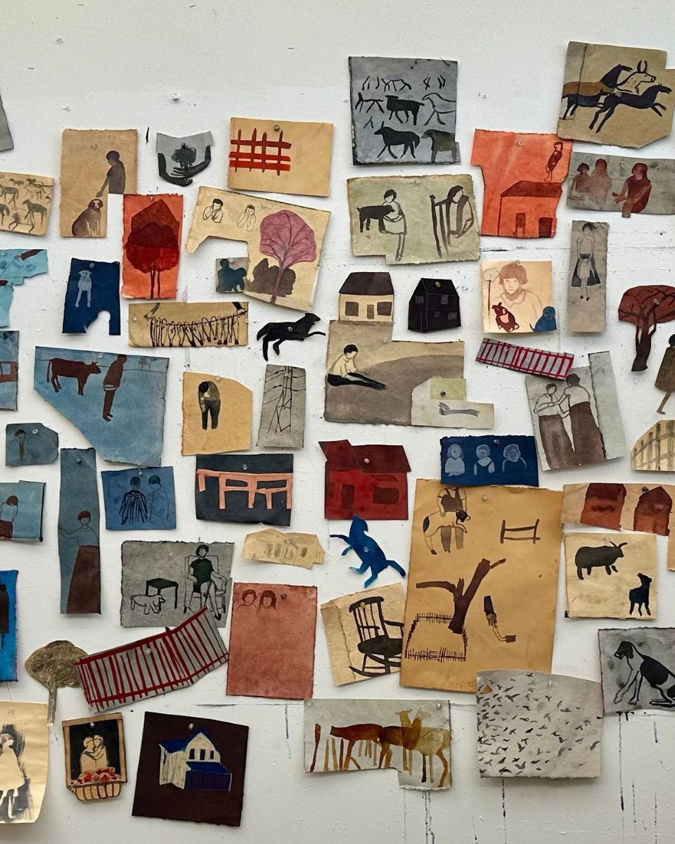 Vertical view of a studio wall covered in dozens of small paper drawings, figure studies, and animal sketches.