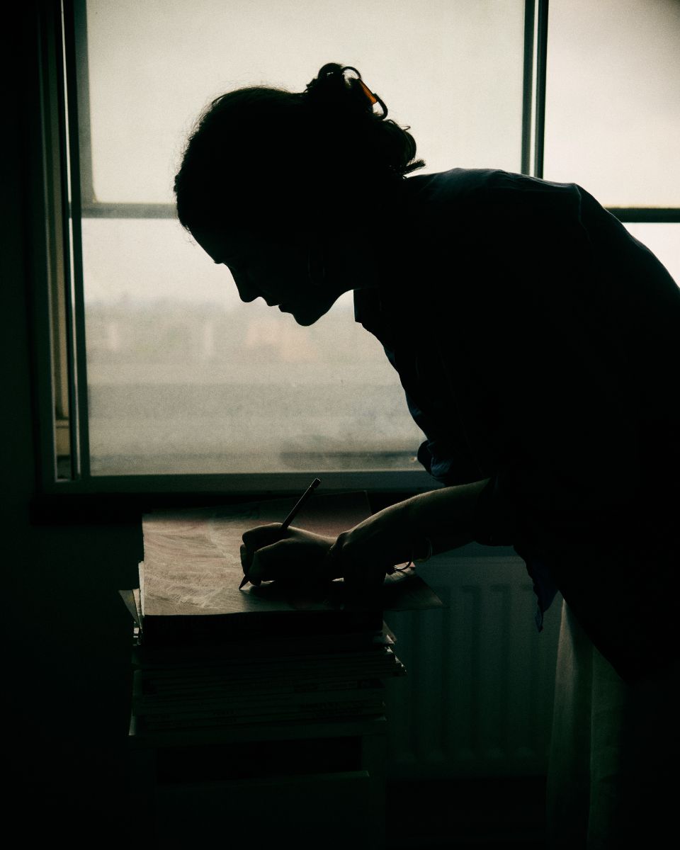 A moody shadow silhouette portrait of contemporary artist Keziah Mornin at work projected against her studio window.