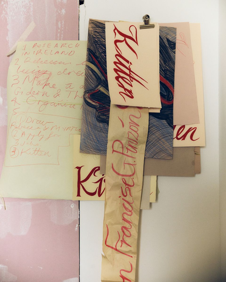 Artist process notes, font lettering tests, and sketches held together by a wall clip in Keziah Mornin’s studio.