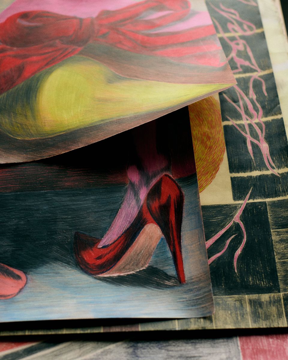 Layered colored pencil drawings depicting a sharp red stiletto shoe and an intricate bow in Keziah Mornin’s studio.