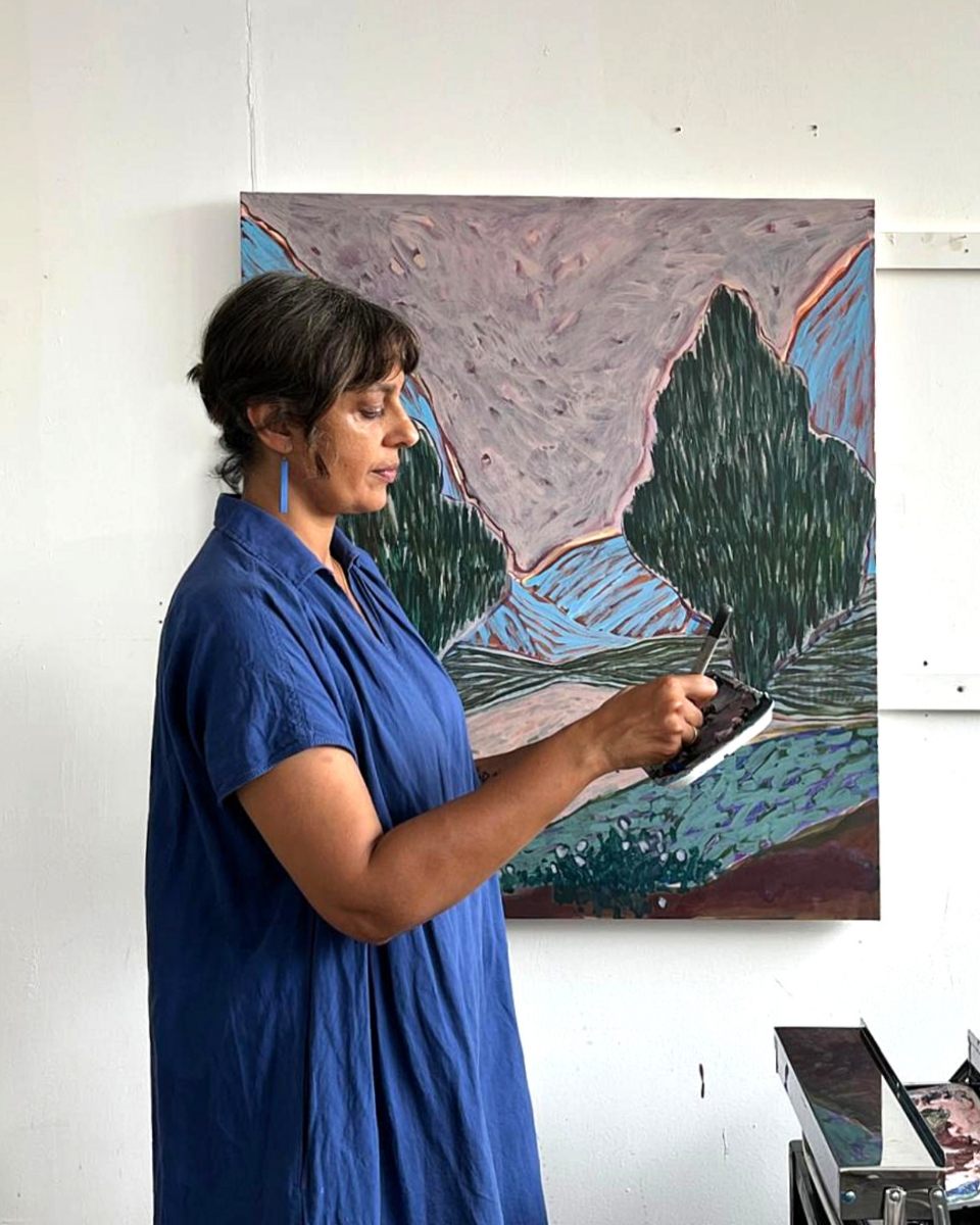 A side profile portrait of artist Kulbir Bhandal in her studio in front of an abstract landscape painting.