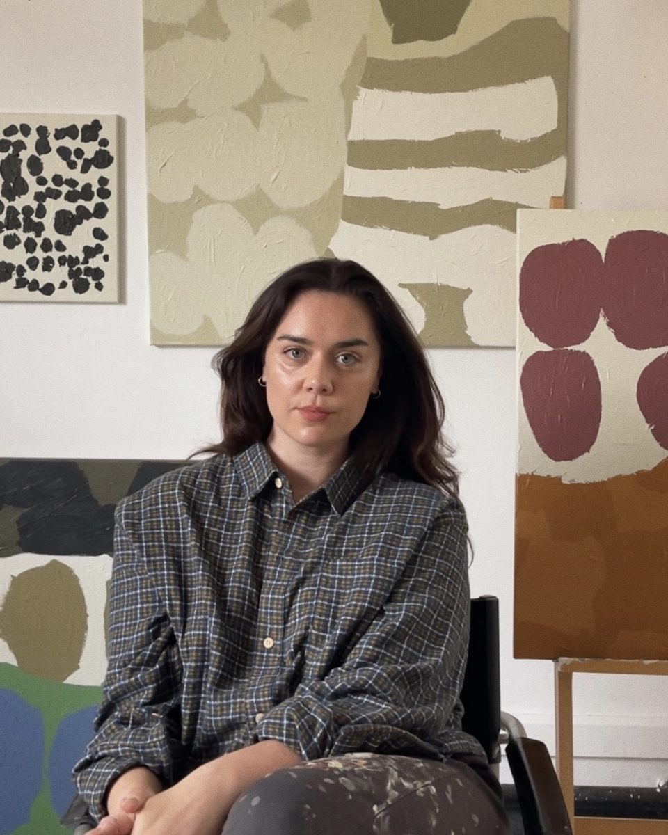 Artist Laurie Maun sitting in her studio in front of her abstract paintings for Partnership Editions.