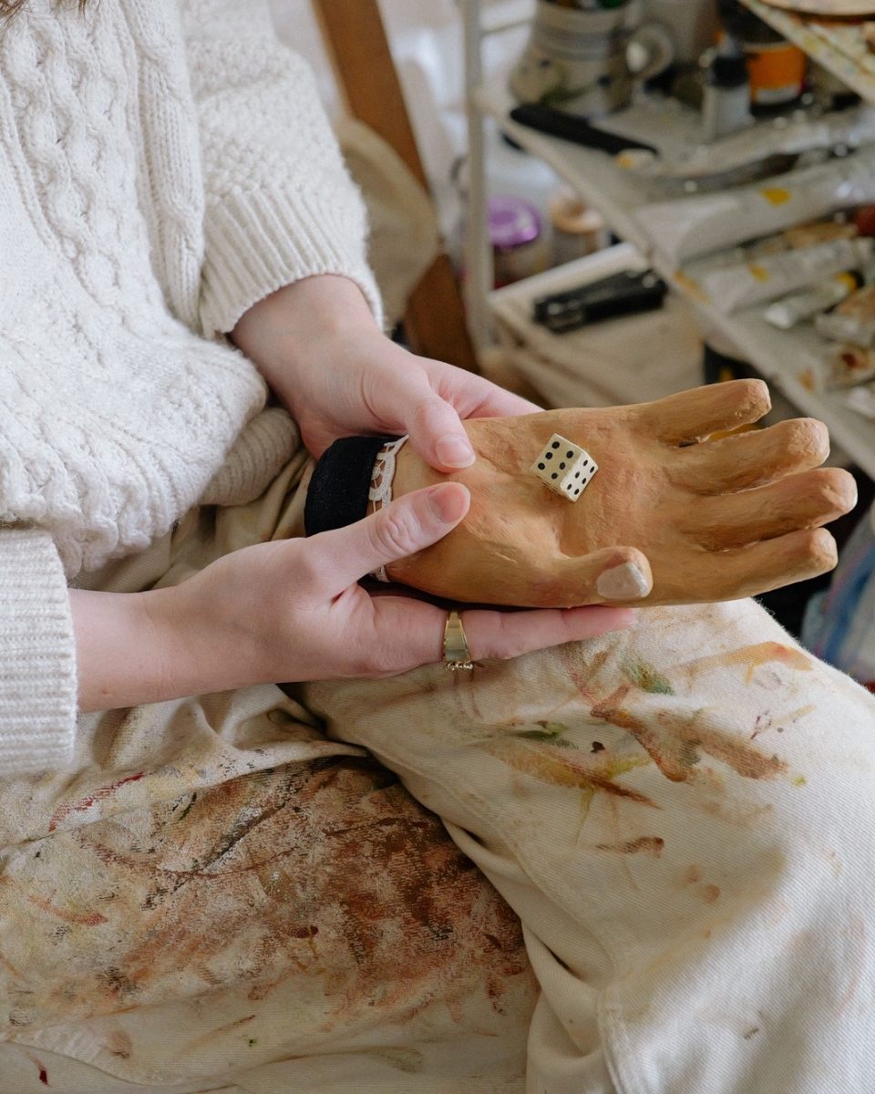 Lily Rose Fine in her studio holding a sculptural hand and oversized dice, bridging the gap between her paintings and 3D emblems.