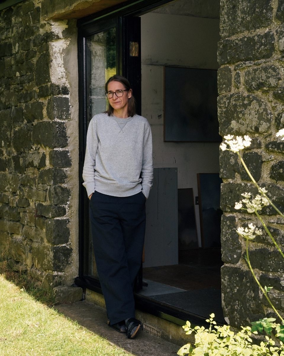 Lisa Hardy leaning against her converted barn studio entrance, an intimate portrait of the artist in her rural Welsh surroundings.