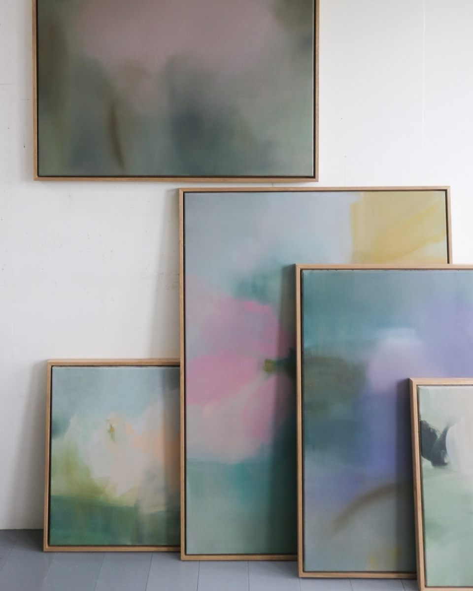 A styled series of wood framed Lisa Hardy paintings arranged on the wall and floor in a minimalist studio.
