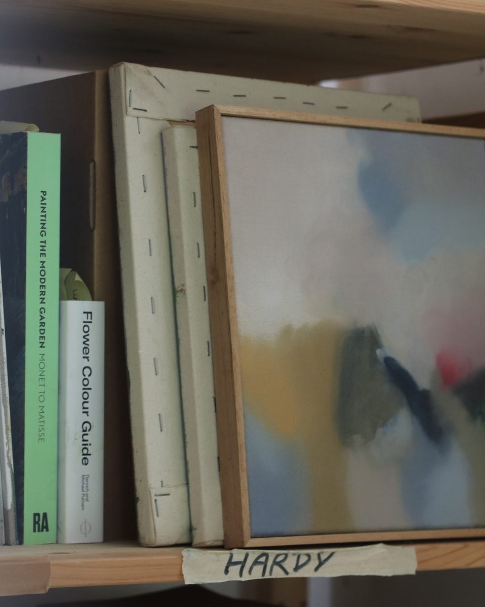 Lisa Hardy's studio bookshelf displaying framed and unframed abstract paintings stacked with inspiration books.
