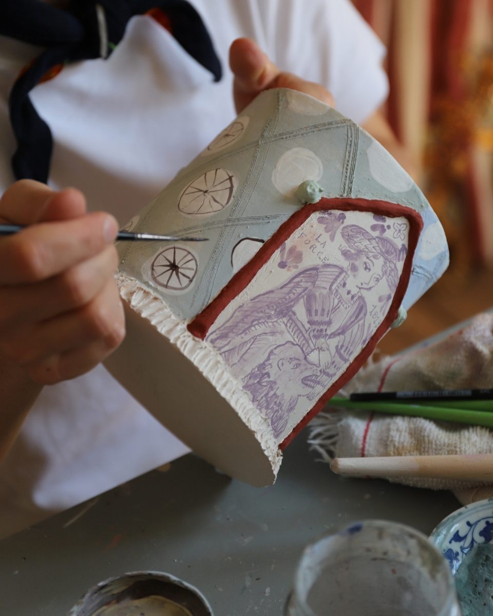 Close-up of Lisa Sandner delicately applying illustrative hand-painted details to a stoneware vase in her Münster studio.