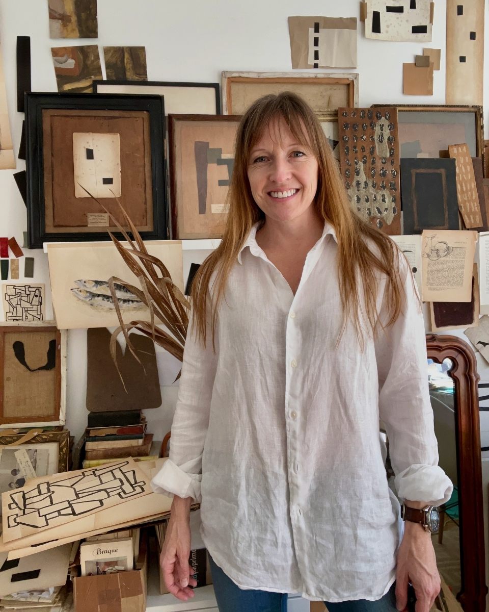Artist Lucy Naughton posing in her studio in front of a shelf filled with framed abstract artwork frames and sketches.