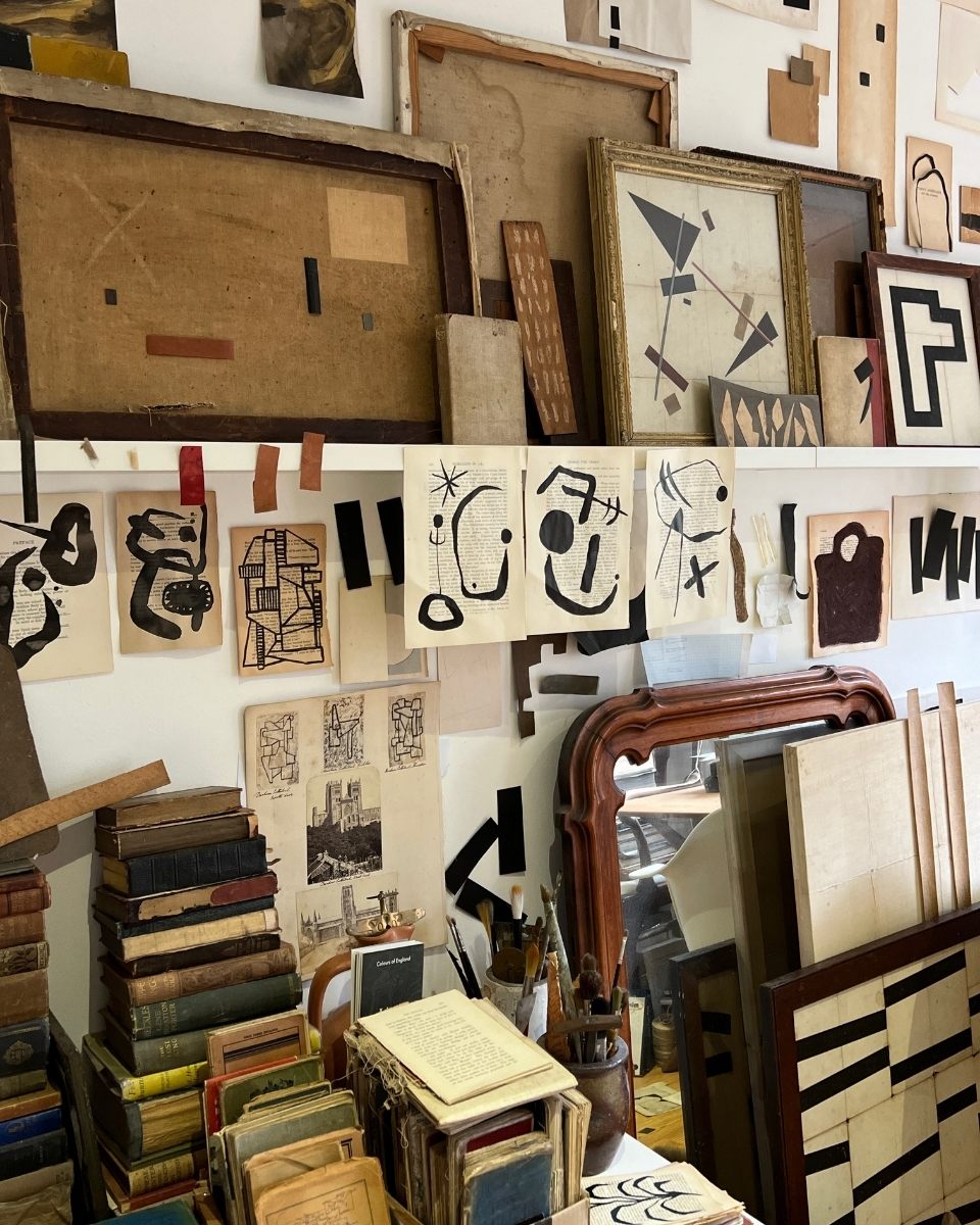 Wide-shot of Lucy Naughton’s studio wall, a dense arrangement of framed works, drawings, and art books that inform her graphic aesthetic.