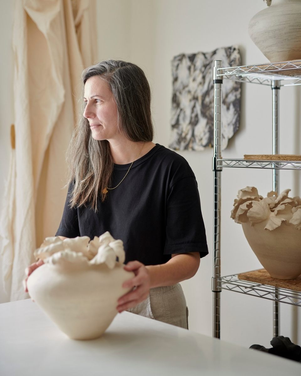 Lucy Whitford portrait holding a hand-built, organic-shaped white sculptural bowl, showcasing the tactile texture of her stoneware.