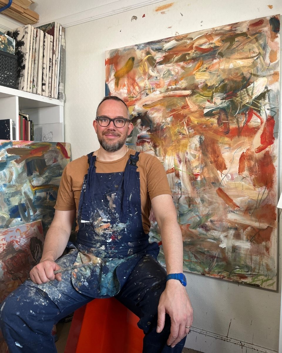 Artist Maarten van den Bos sitting in his London studio in front of a large abstract expressionist painting.