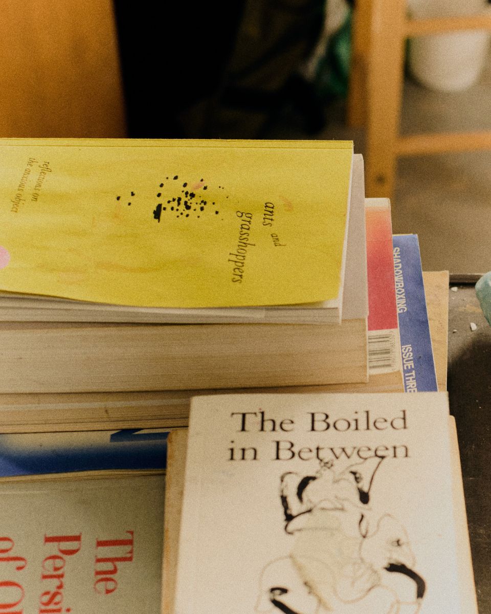A clean, styled shot of contemporary art and research reference books stacked inside Mae Nicolaou's studio.