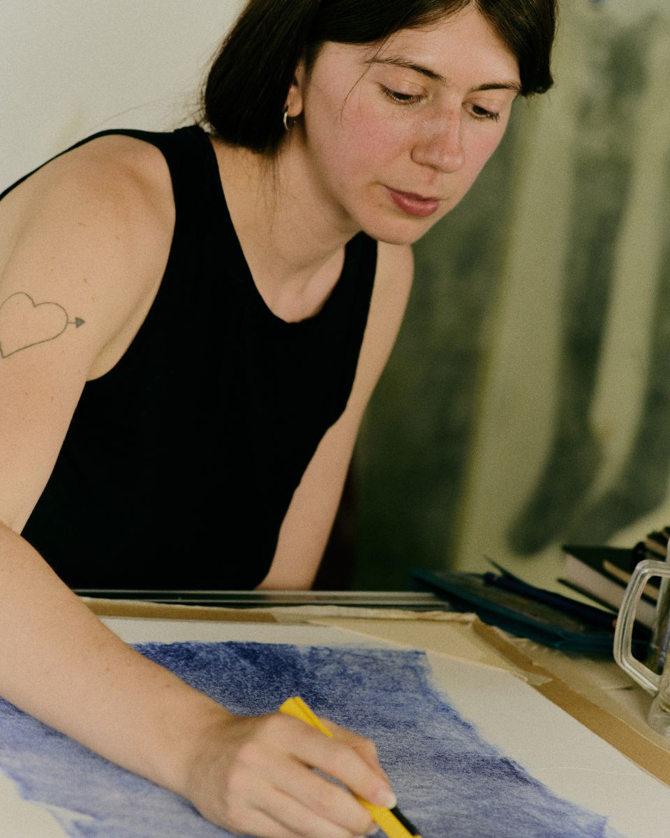 Mae Nicolaou at work drawing and constructing an intricate paper artwork at her studio desk.