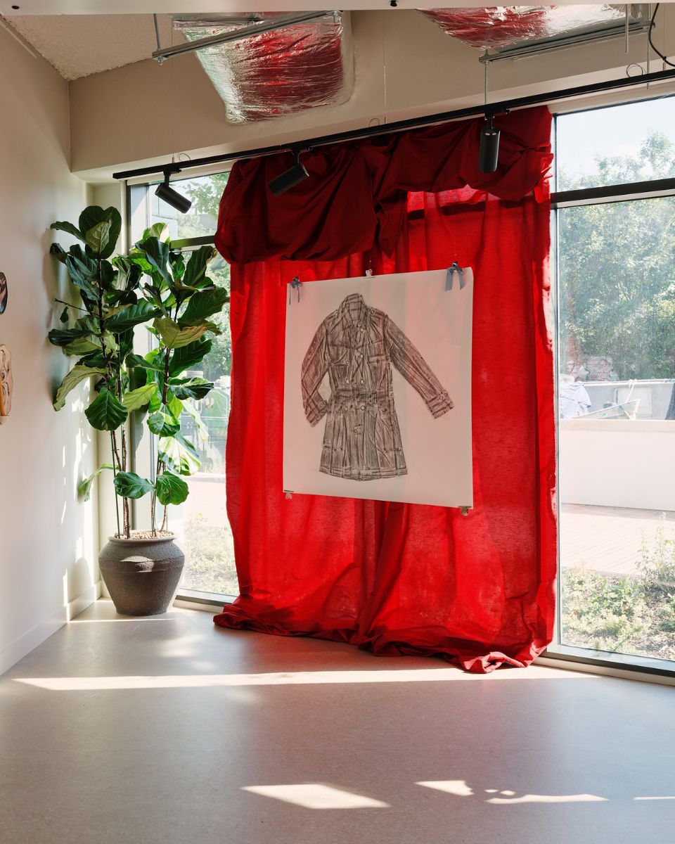 An intricate frottage textured drawing by Mae Nicolaou, hanging in front of a red curtain for the Partnership Editions Dressing Up exhibition.