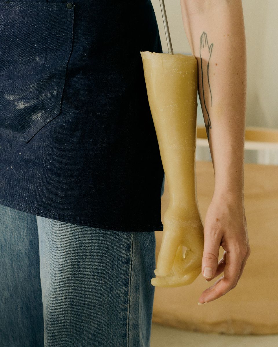 A detailed studio shot of a realistic wax arm cast sculpture held next to Mae Nicolaou’s own arm.