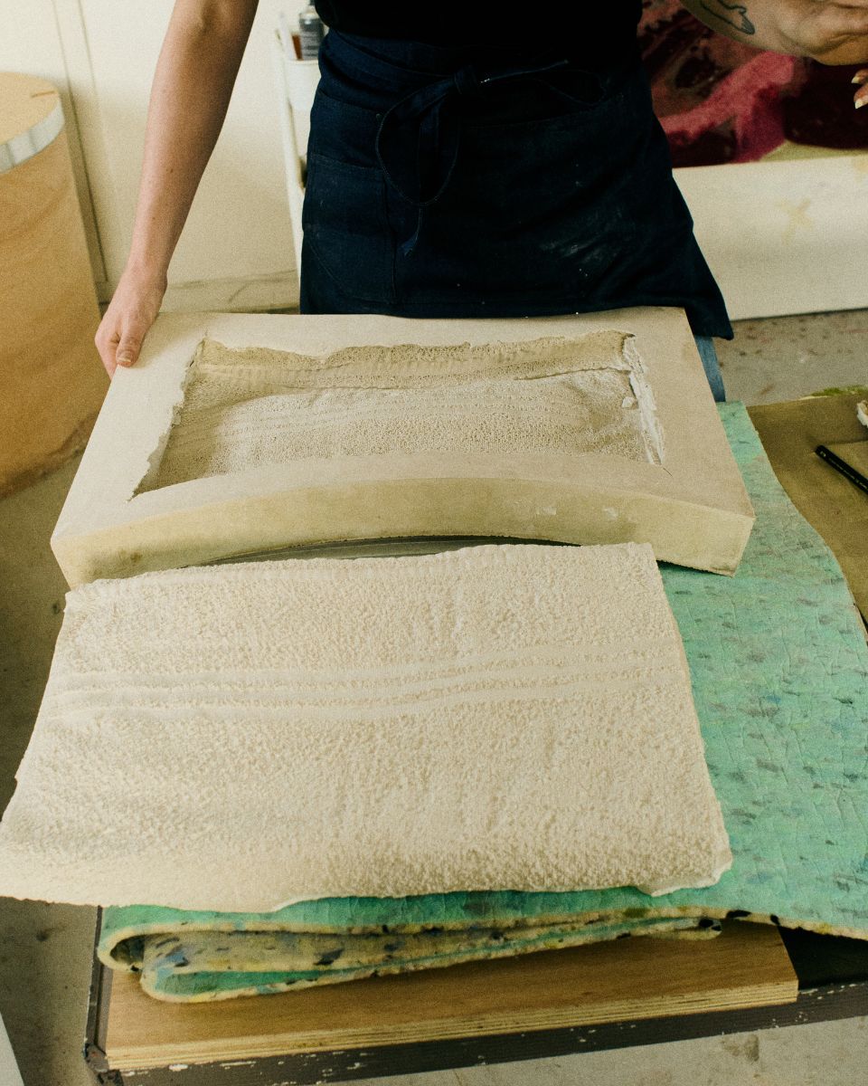 Mae Nicolaou holding a large textured open cast sculpture piece steady on a work surface in her studio.