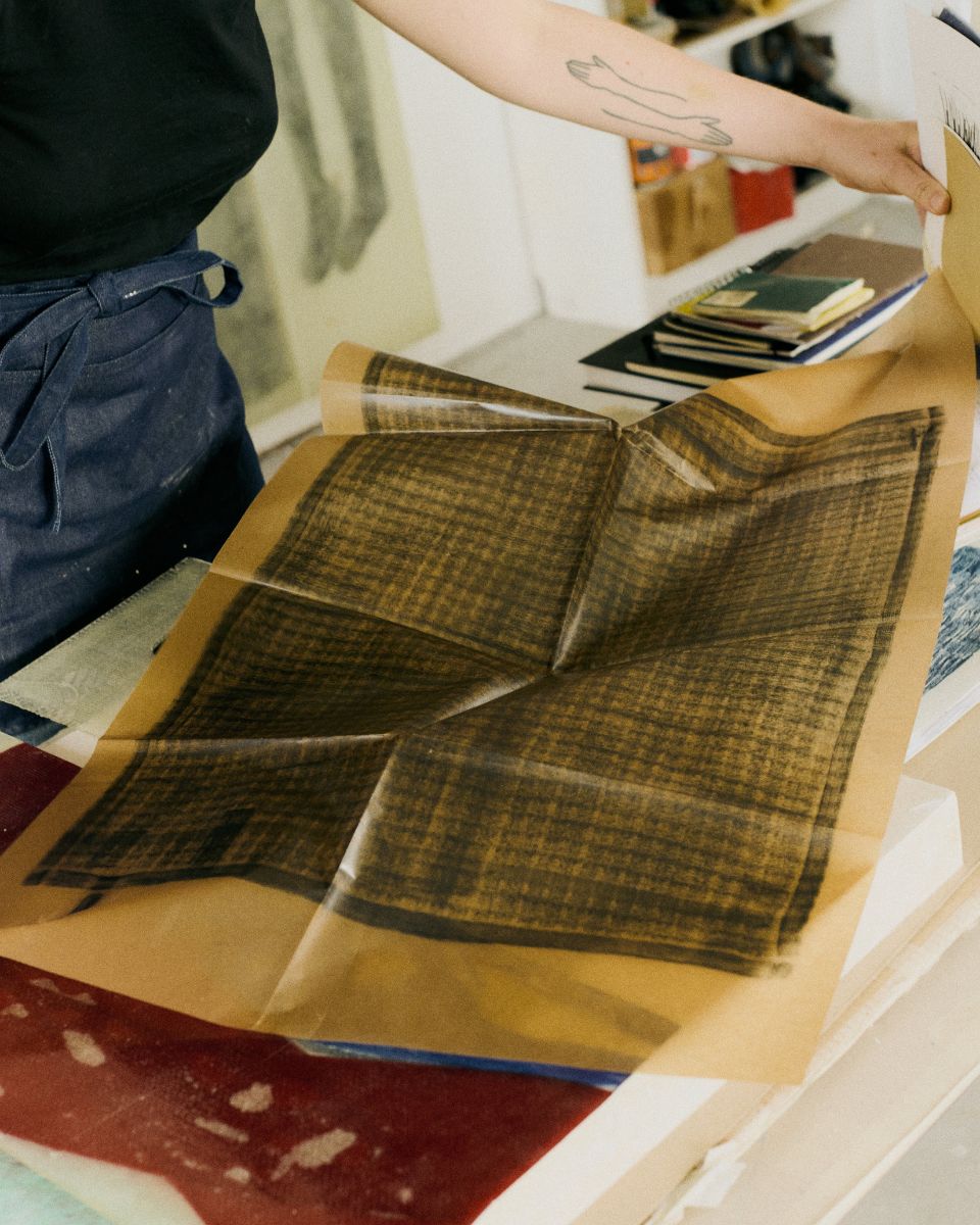Mae Nicolaou unfolding a large-scale print process composition on a table inside her art studio.