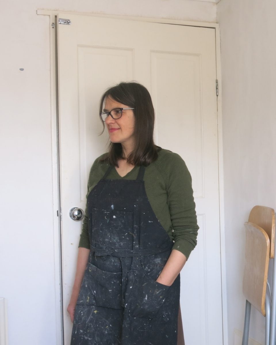 Artist Mandy Hudson posing in an indoor portrait directly in front of her white modern studio door.