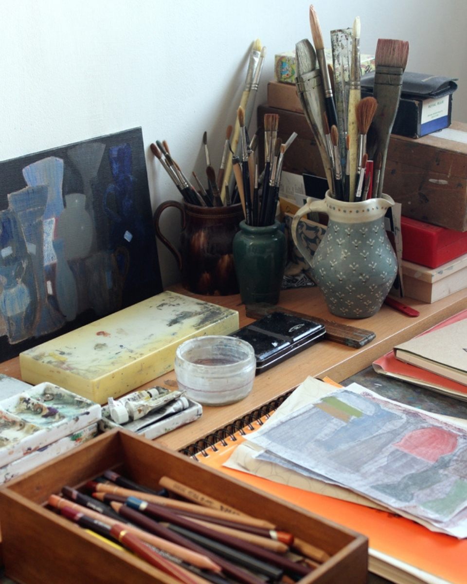Close-up of Mandy Hudson’s studio desk, organised with drawing pencils, preliminary sketches, and professional oil paints.