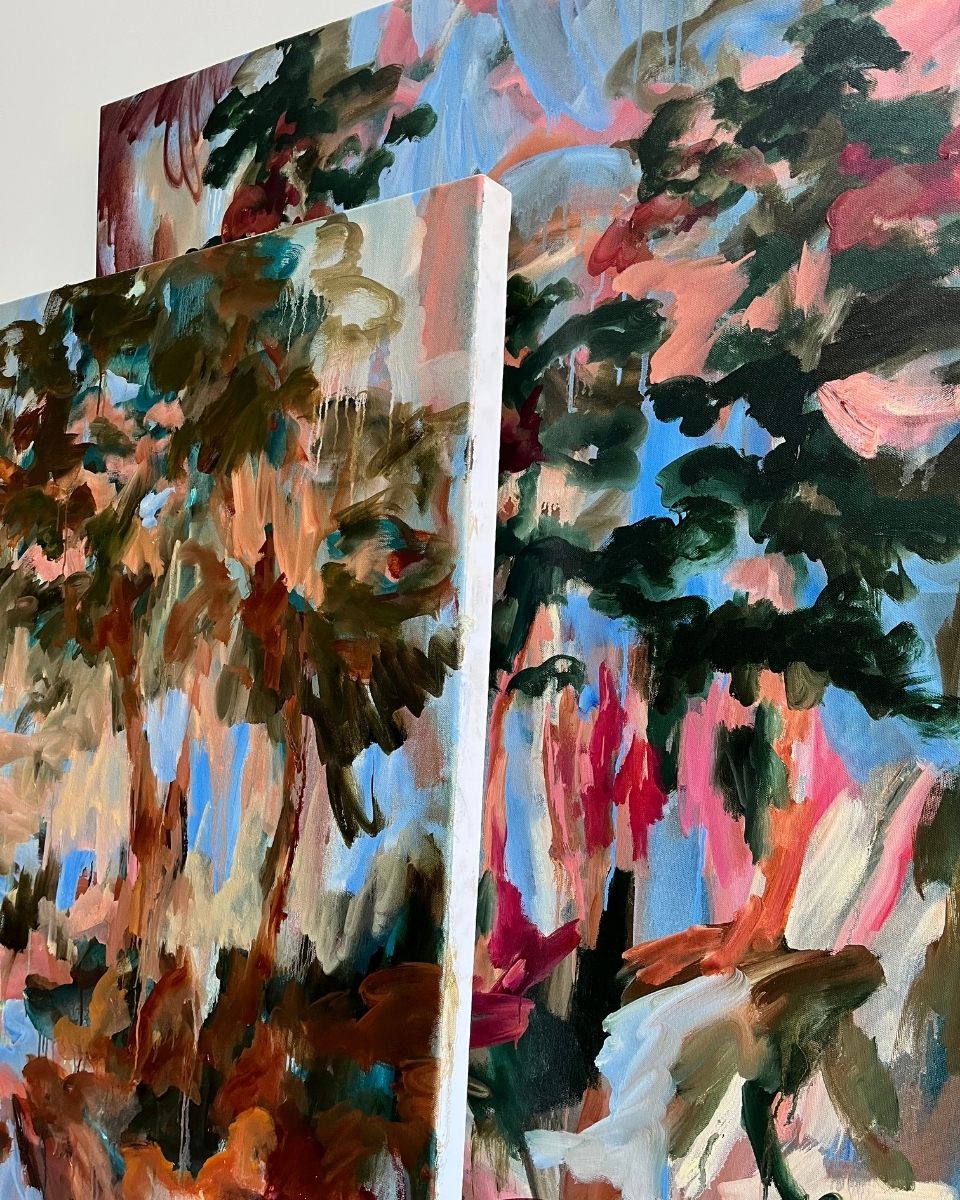 Close-up detail of two Mary West oil paintings leaning together, showcasing her textures and layered forest-inspired palettes.