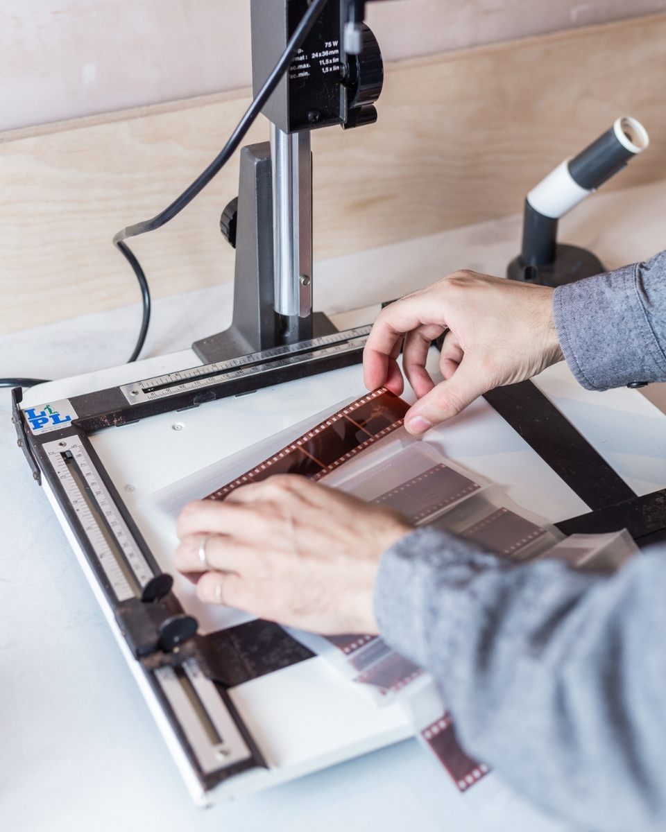 Close-up of Matt Ritson’s hands placing film negatives on an enlarger’s workspace in his studio.