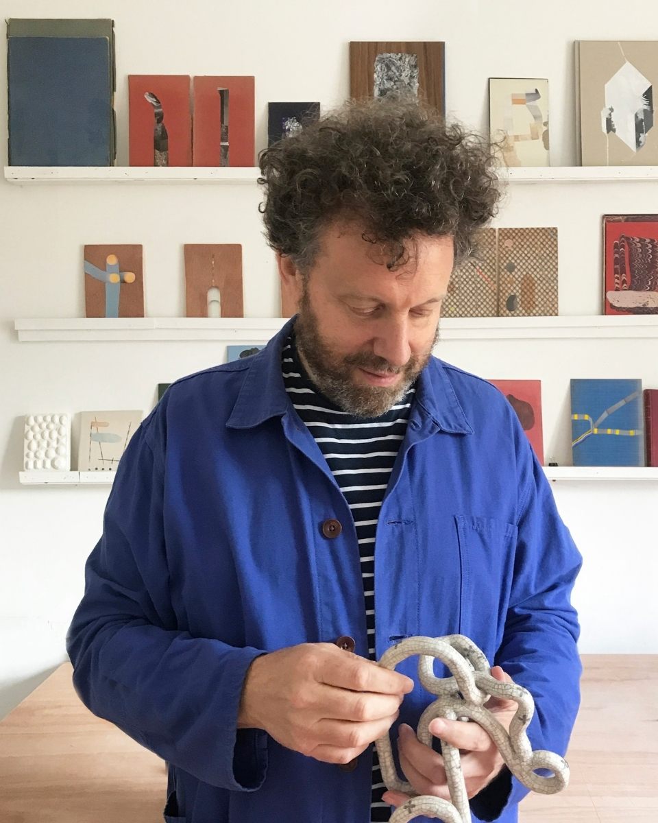 Artist Matthew Richardson in front of studio shelves displaying his small-scale abstract artworks.
