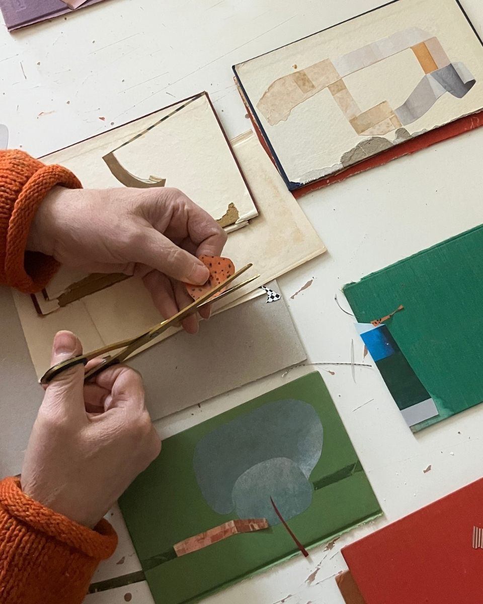Close-up of artist Matthew Richardson’s hands using scissors to carefully cut elements for a new mixed-media collage.