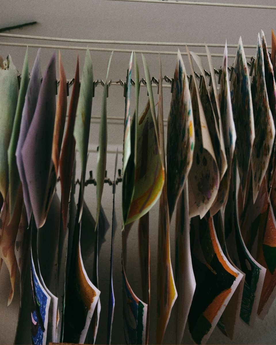 Detail shot of Max Freund’s studio drying process, featuring original works on paper suspended by clips on a string.