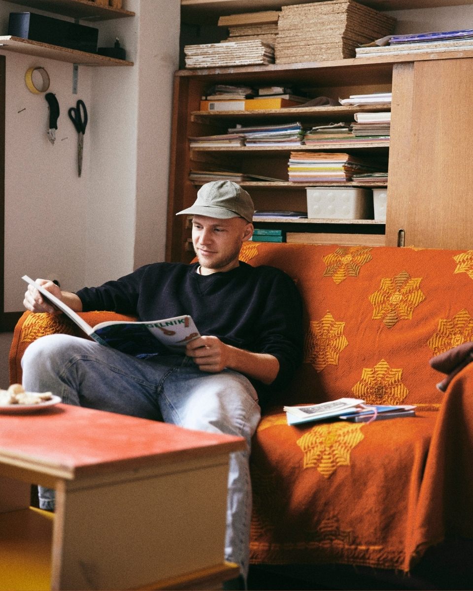 Max Freund seated on a studio sofa, flicking through reference imagery that informs the motifs in his work.