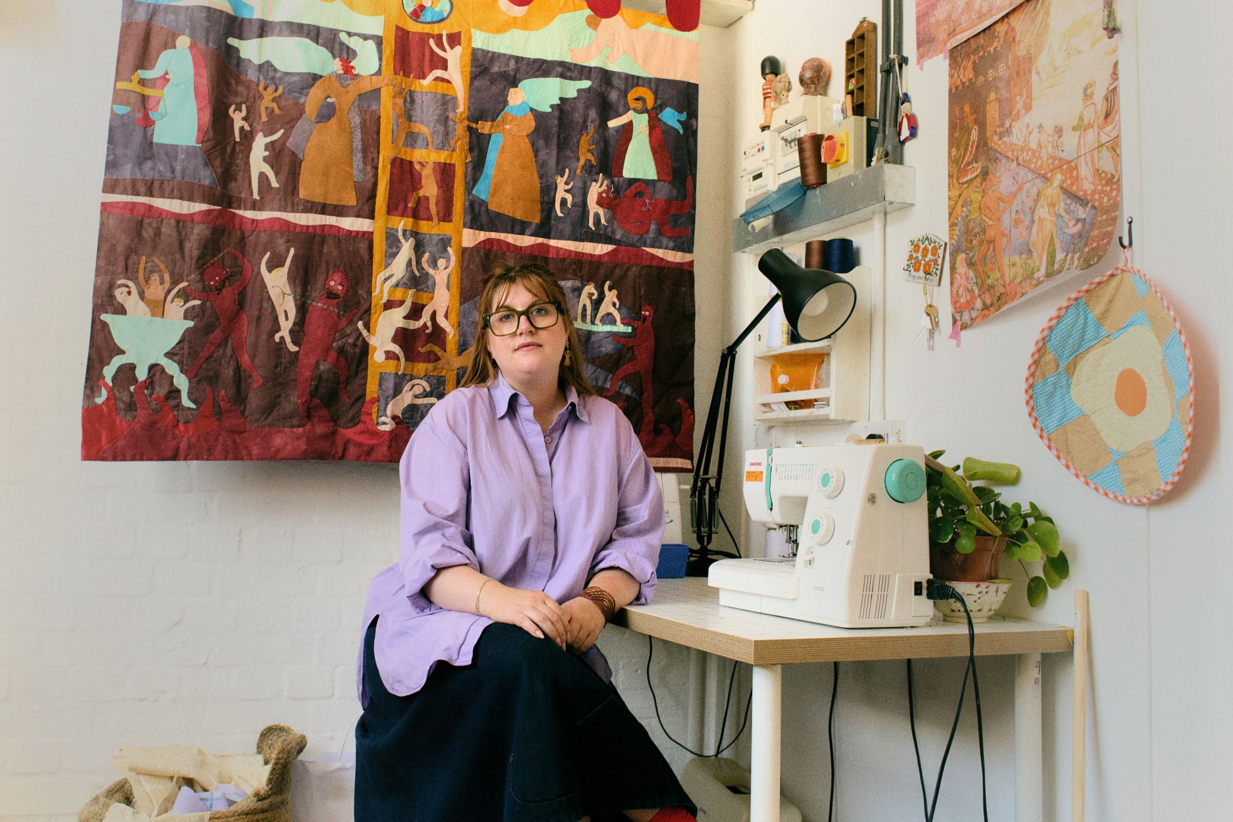 Seated portrait of artist Molly Lester in her studio surrounded by her colourful textile artwork.