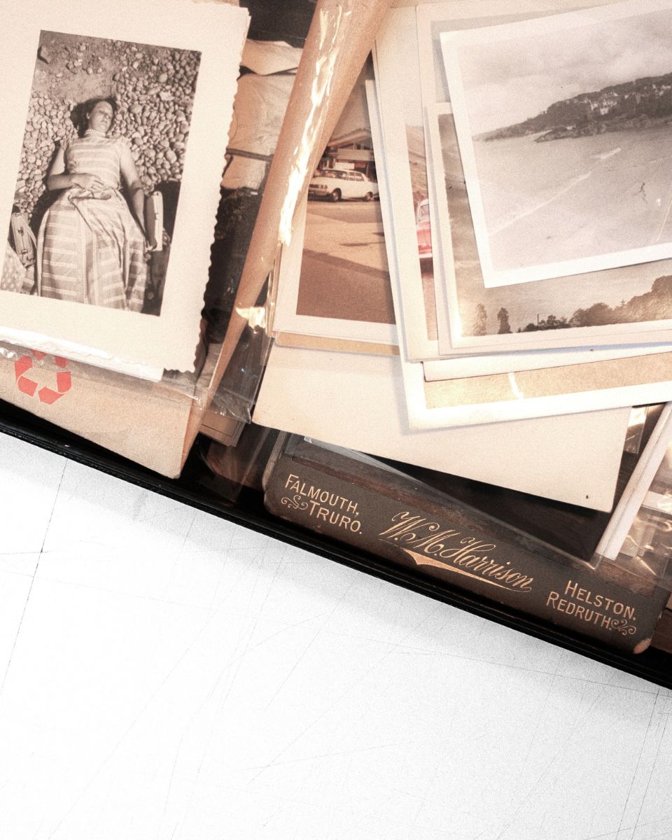 Vintage black and white family photographs and seaside postcards arranged on a glass table by Mona Sultan for Partnership Editions.