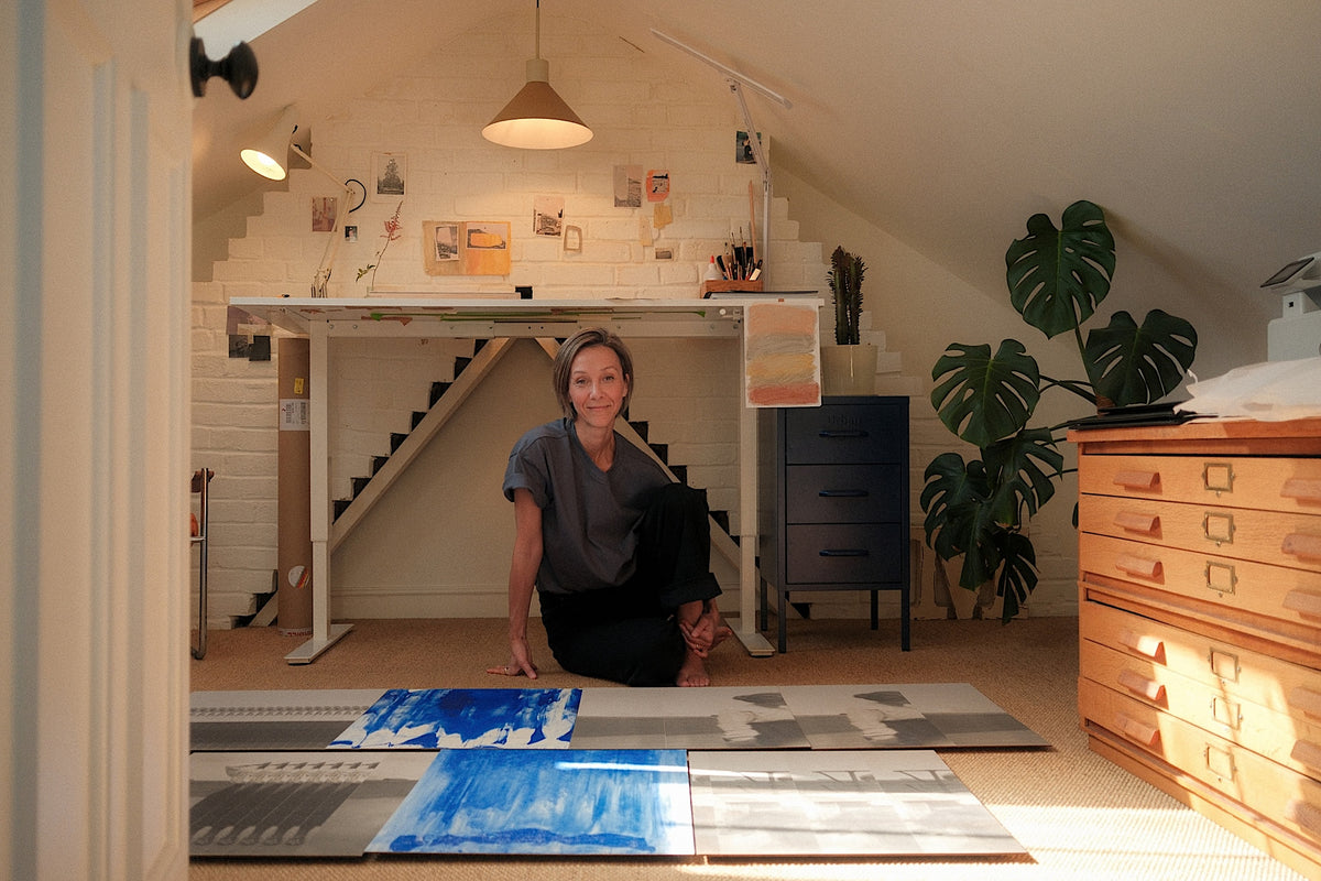 Artist Mona Sultan sitting cross-legged on the floor of her loft studio surrounded by laid-out blue and sepia photographic prints for Partnership Editions.