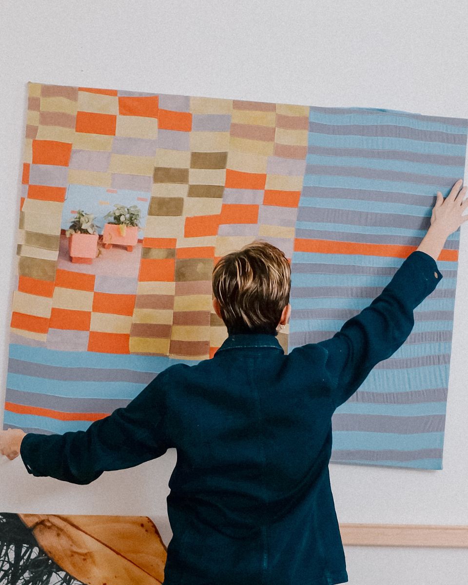 Nathalie Basoski arranging a mixed-media stitched piece on her home studio wall.