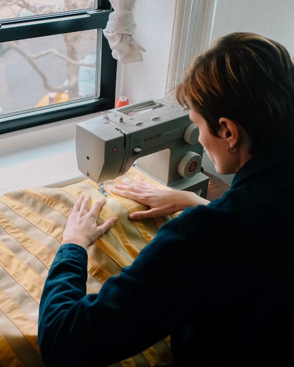 Nathalie Basoski in her London studio, using a sewing machine to create precise gestural lines on a mixed-media textile artwork.