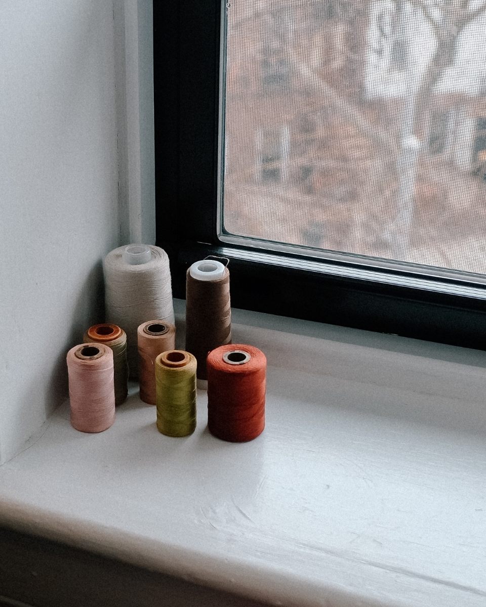 Detail shot of vibrant spools of thread on Nathalie Basoski’s studio window sill, essential tools for her textile-based abstractions.