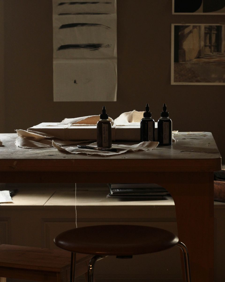 Three glass dye bottles and natural linen fabric resting on a wooden studio workbench.