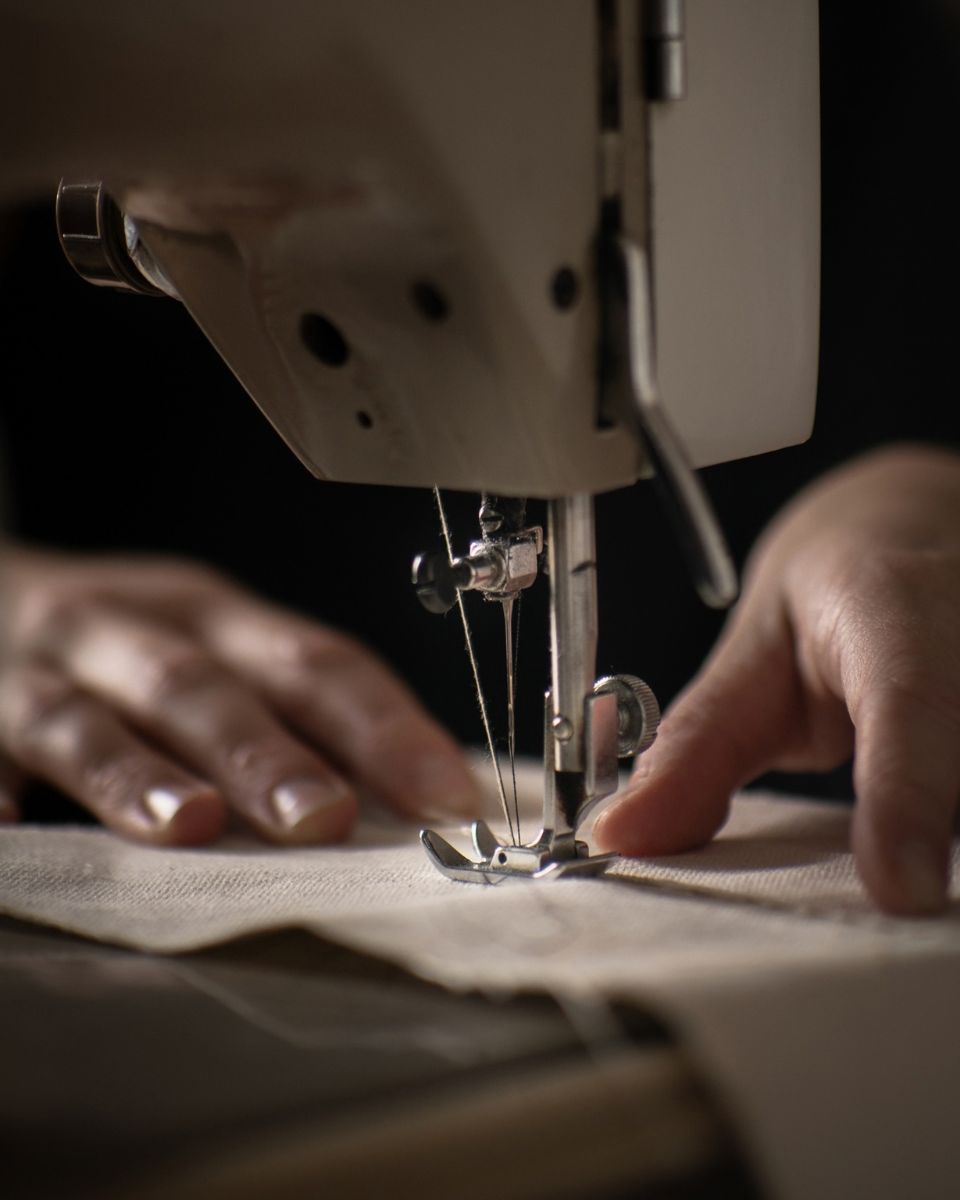 Macro close-up of artist hands stitching natural canvas fabric under a sewing machine needle.