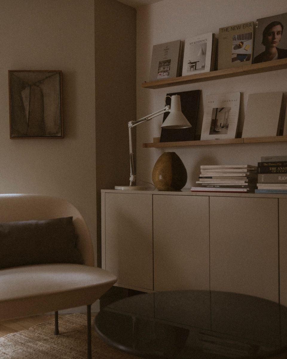 Minimalist studio interior featuring a modern armchair, wooden shelving with art books, and a cream sideboard.