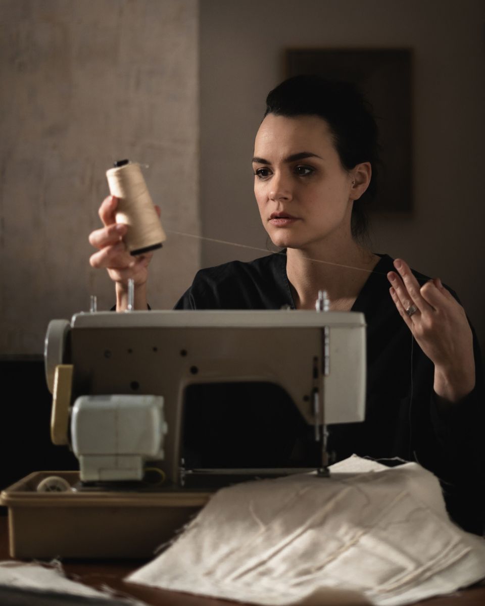 Textile artist Nikki Heaton threading cream spool thread into a vintage sewing machine at her studio desk.