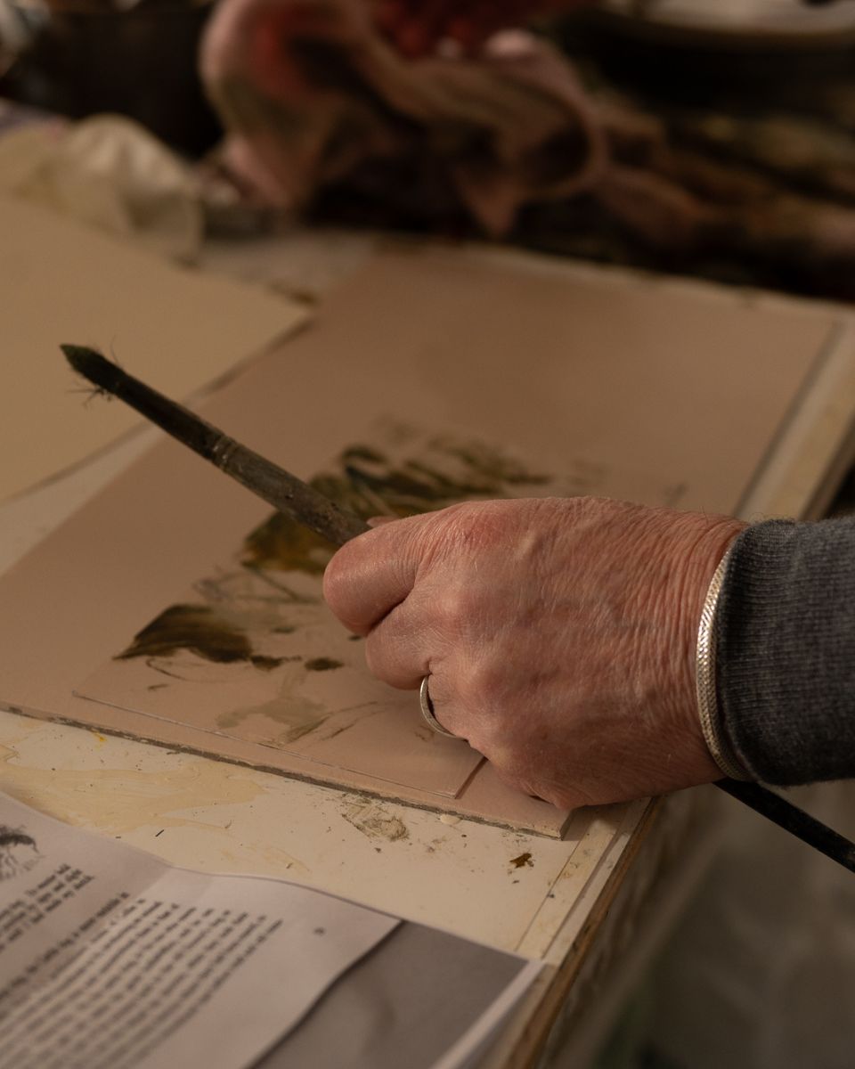 Close-up of artist Philip Maltman holding a thin paintbrush and applying olive green strokes onto paper in his studio.
