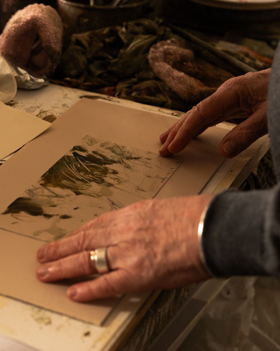 Artist Philip Maltman's hands carefully adjusting a small, freshly painted landscape artwork on a studio tabletop.