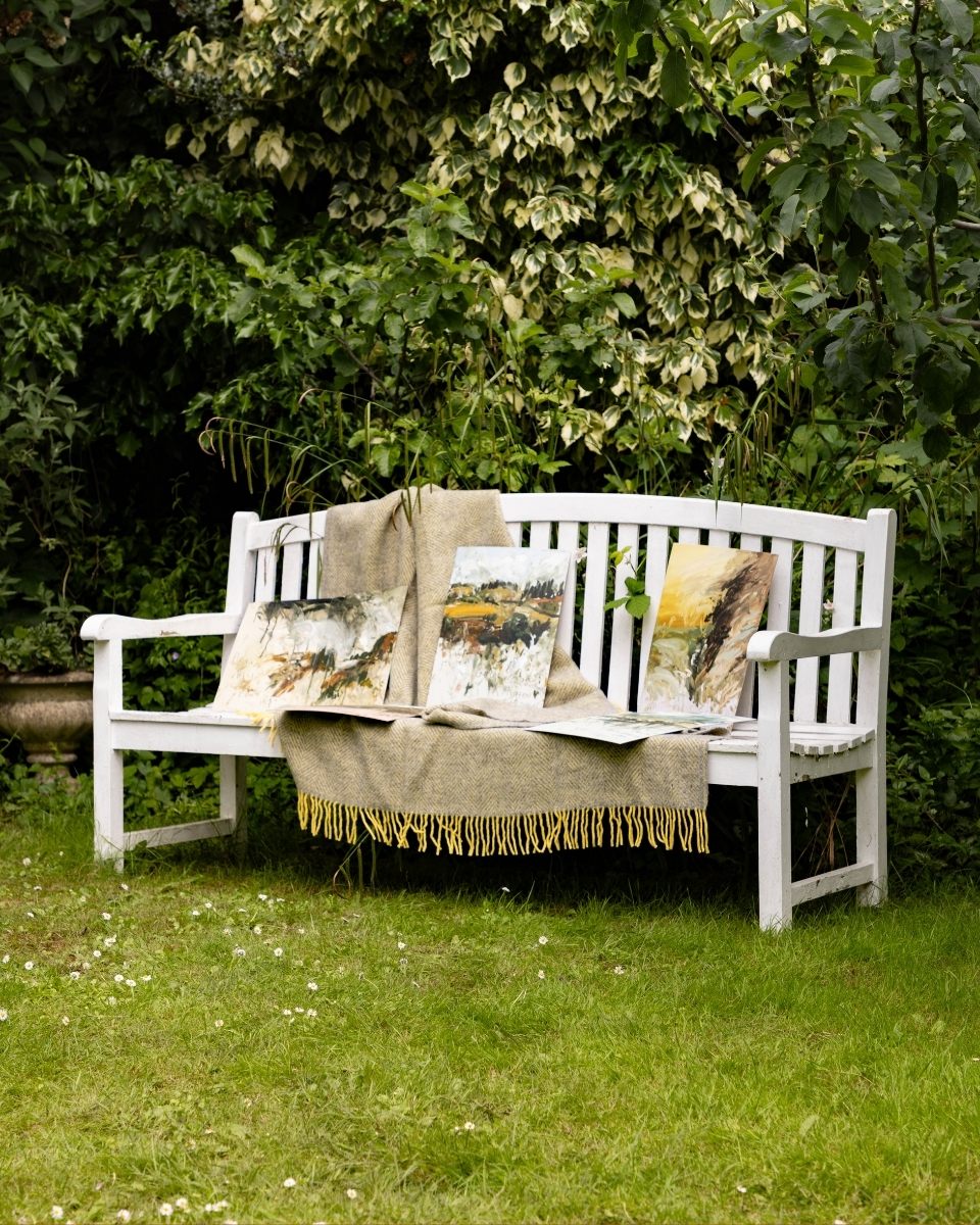 A collection of Philip Maltman’s abstract landscape paintings displayed on a wooden garden bench in soft, natural daylight.