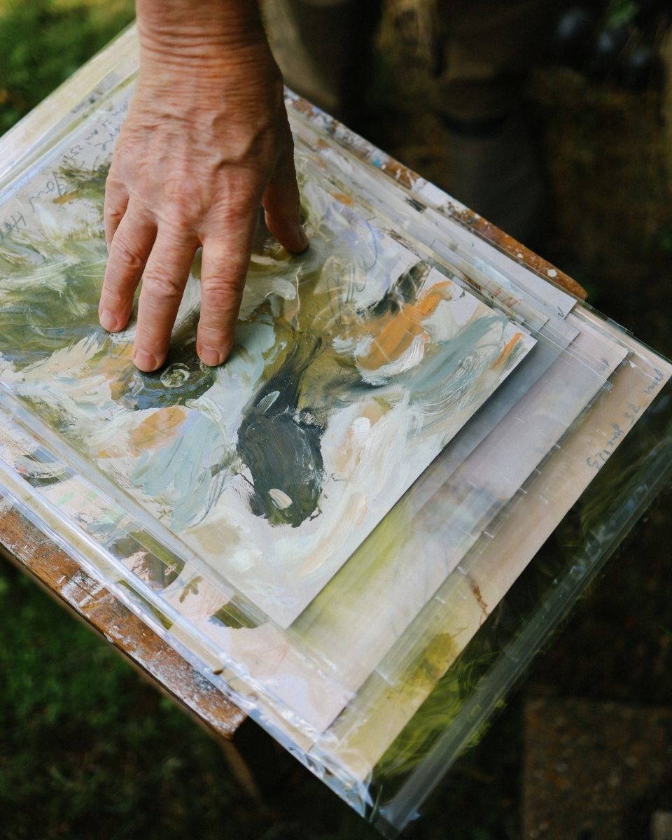 Close-up of artist Philip Maltman's hand pressing down on small-scale artworks stored in plastic sleeves.